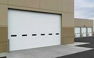 A large white flush overhead door with a row of small windows in a tan commercial building.